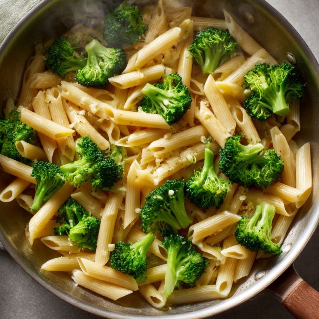 Penne pasta and broccoli being mixed together in a skillet for chicken broccoli pasta.