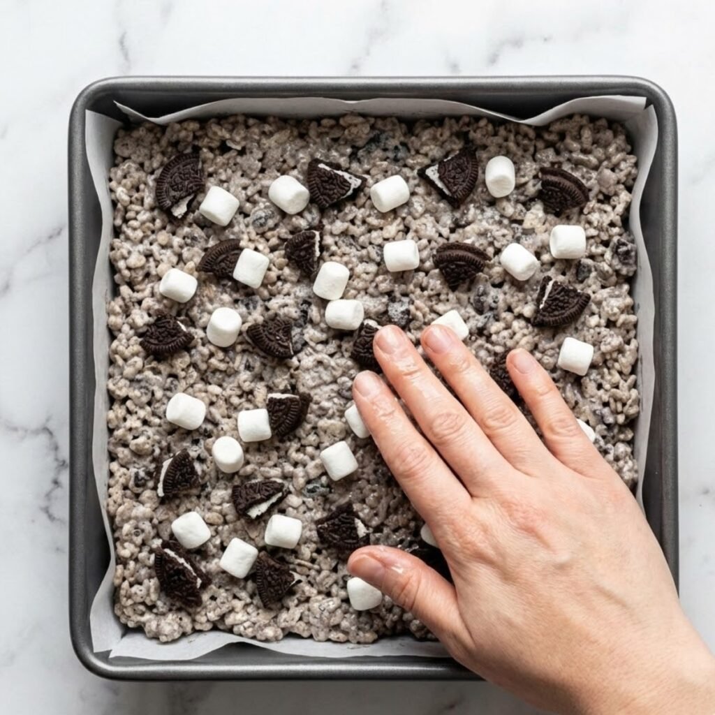 Gently press the sticky Oreo Krispie mixture into a parchment-lined pan, topping with extra cookies and marshmallows for a bakery-style finish. Do not pack tightly.