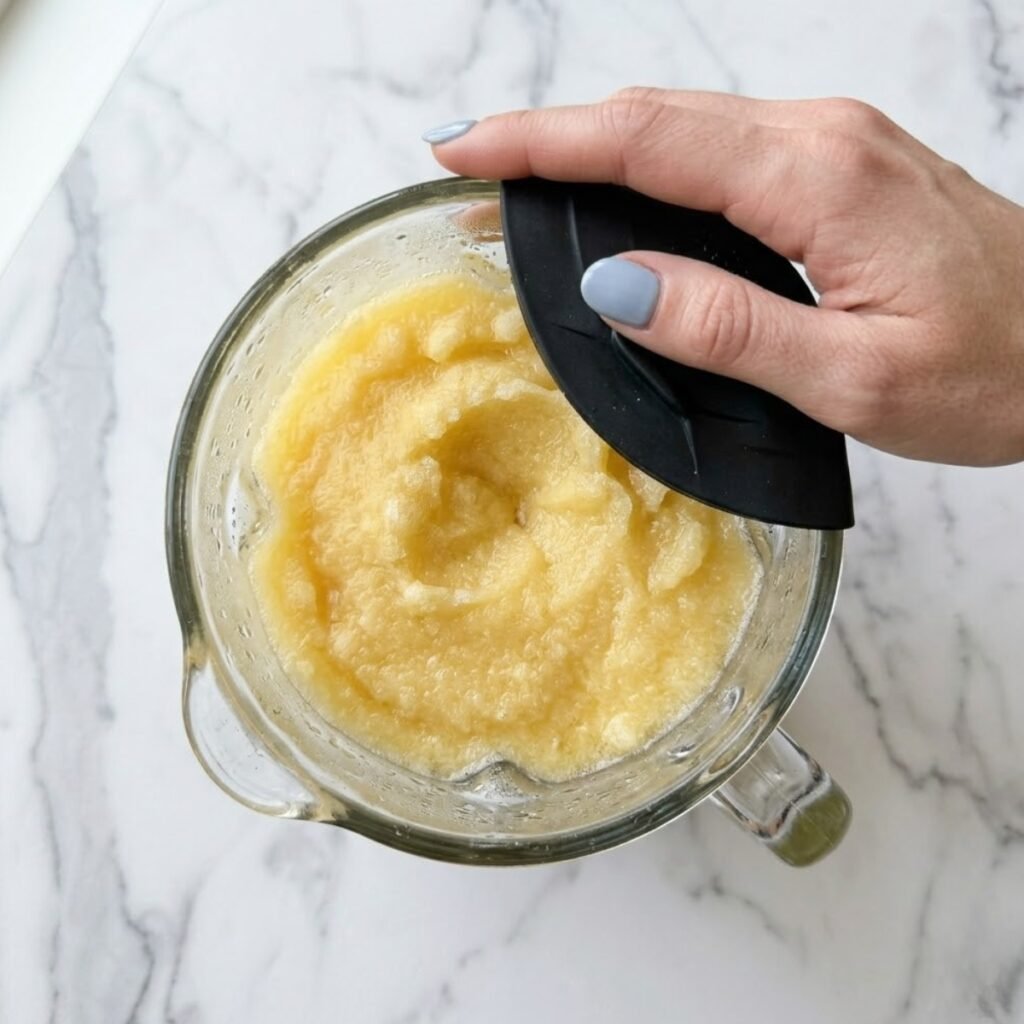 A high-speed blender being used to process frozen pineapple and juice into a thick, golden, frosty slushie texture.