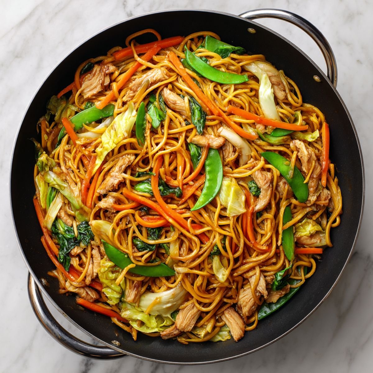 Chicken lo mein with soft golden noodles, tender chicken pieces and colorful vegetables in glossy soy sauce. Authentic Chinese stir fry with carrots, snow peas and cabbage in black wok.