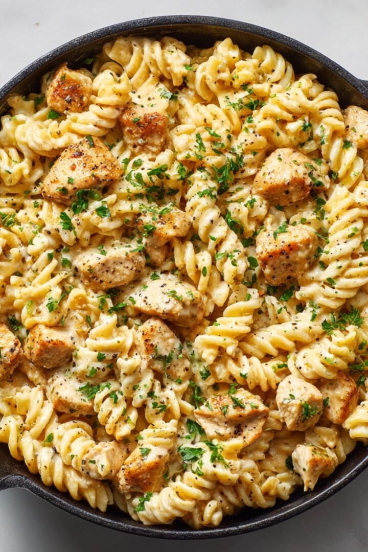 Parmesan chicken pasta with creamy garlic sauce in cast iron skillet topped with fresh parsley. Easy 35 minute one-pot dinner recipe with tender chicken and rotini pasta.