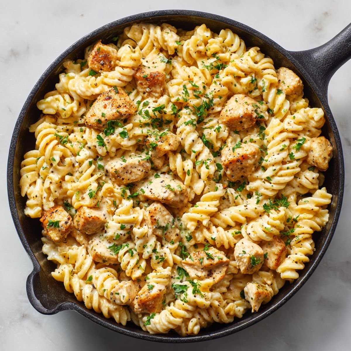 Parmesan chicken pasta with creamy garlic sauce in cast iron skillet topped with fresh parsley. Easy 35 minute one-pot dinner recipe with tender chicken and rotini pasta.