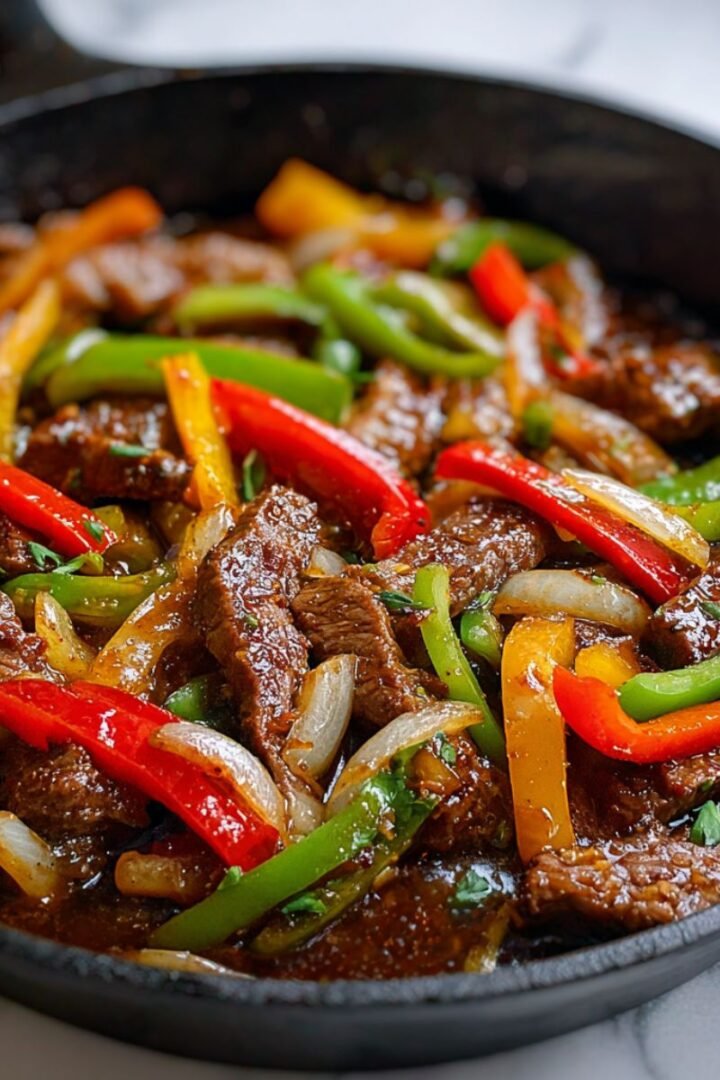 Chinese pepper steak recipe with tender beef strips, colorful bell peppers and glossy brown sauce in cast iron skillet. Authentic restaurant-style stir-fry with perfect sauce coating.