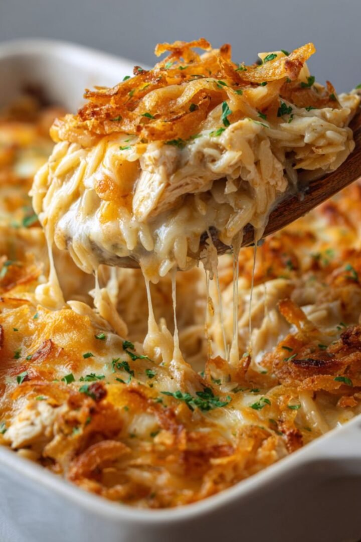 Creamy chicken orzo casserole with melted cheese, tender chicken pieces, and crispy fried onions on top in white baking dish