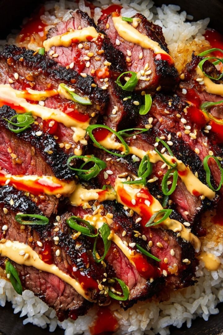 Sliced Korean BBQ steak with creamy sauce and green onions over white rice in black bowl