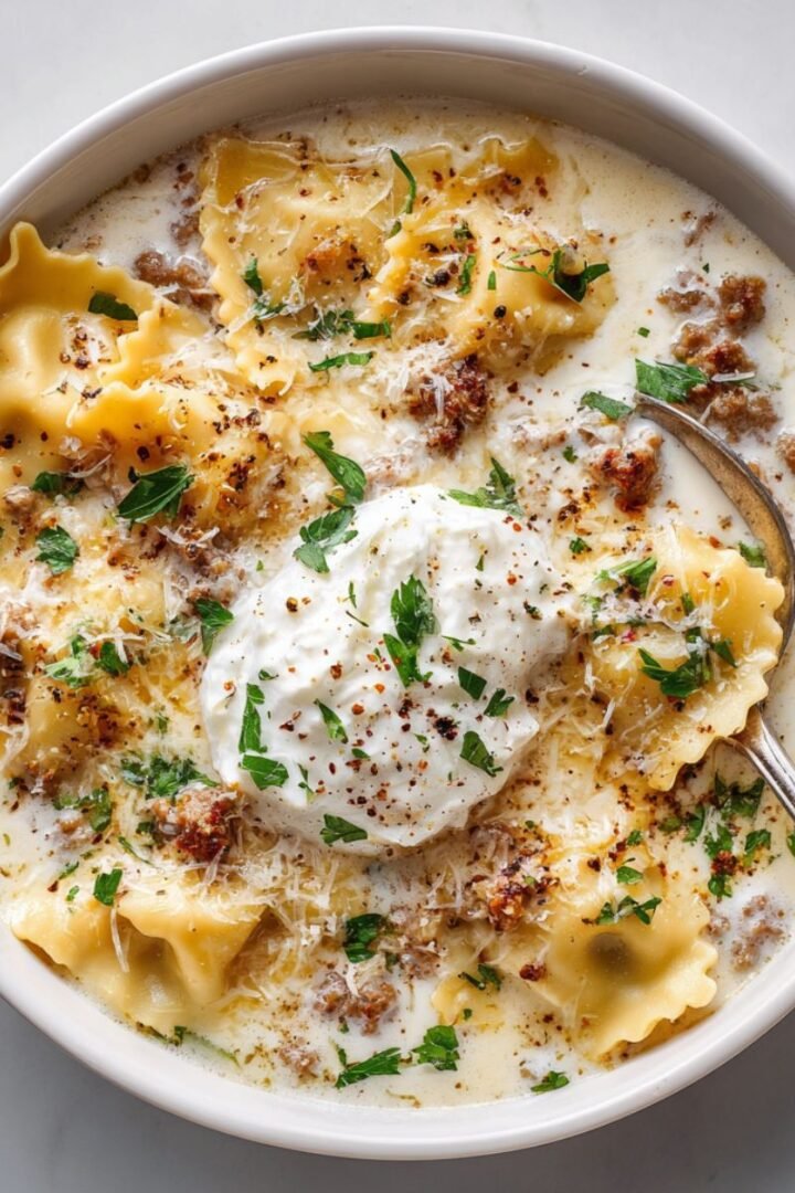 White 35 minute creamy alfredo lasagna soup with tender lasagna noodles floating in rich white Alfredo cream sauce with Italian sausage topped with ricotta dollop and fresh parsley