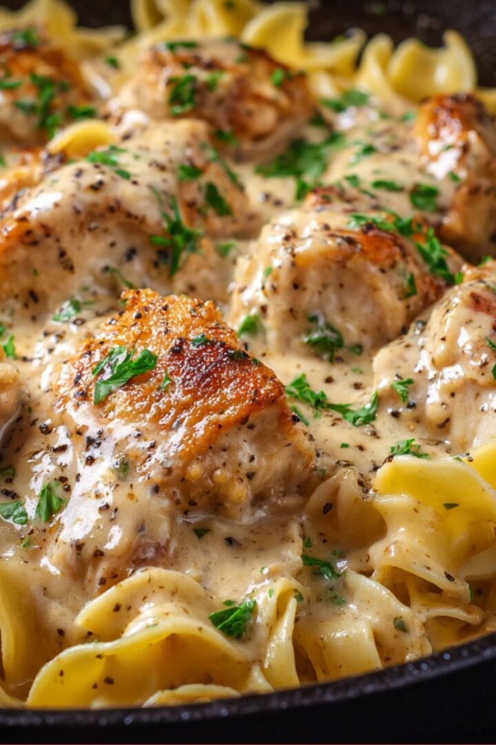 Close-up of chicken with buttered noodles coated in rich creamy garlic sauce.