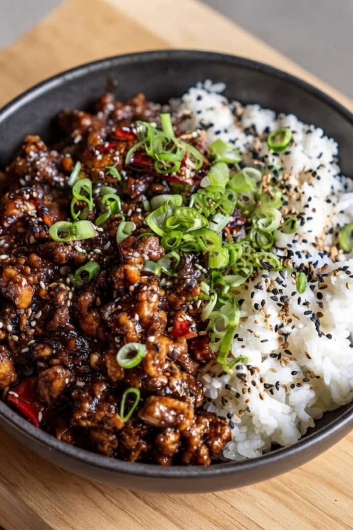 An overhead top-down view of Firecracker Ground Chicken in a black ceramic bowl place on a wooden board, natural lighting.